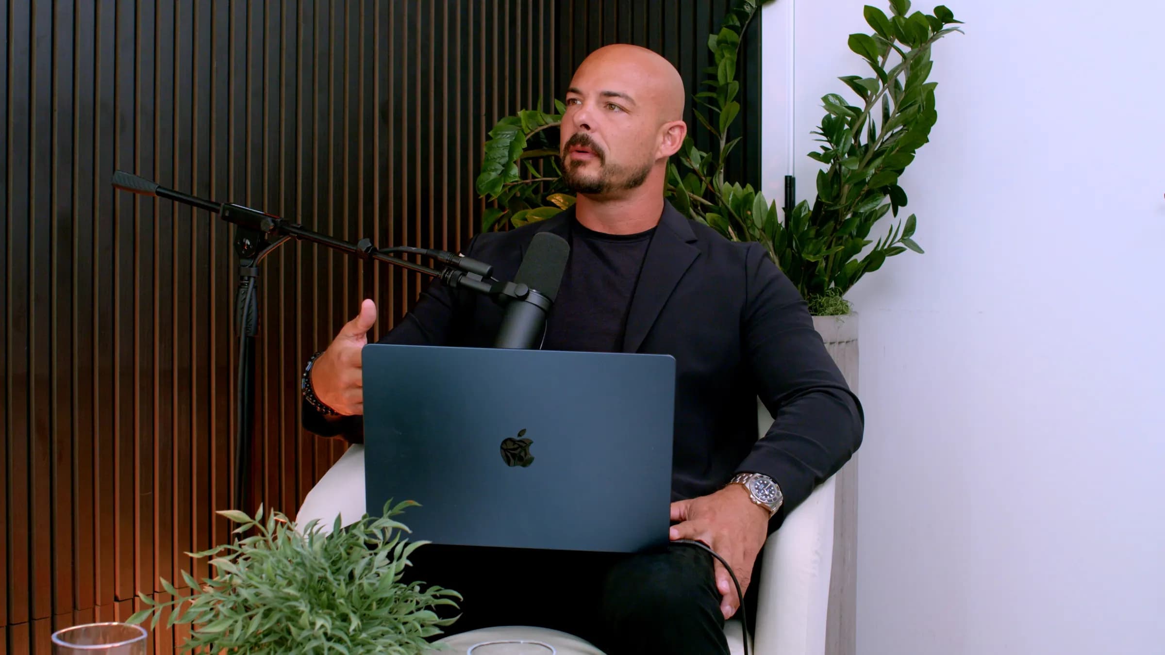 Garin Heslop at a podcast microphone, mid-sentence, a laptop on his knee